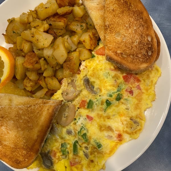 A diner breakfast with a vegetable omelet, home fries, toast, and an orange slice.