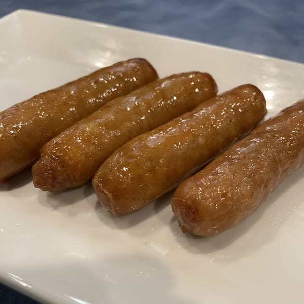 Four glistening brown breakfast sausages arranged diagonally on a white rectangular plate.
