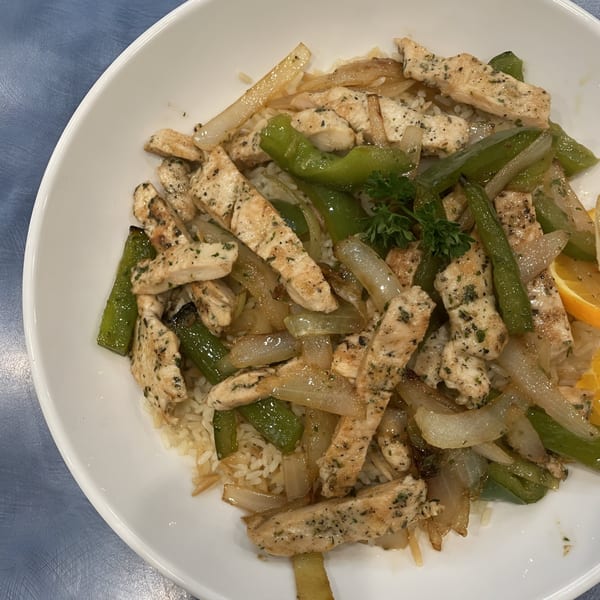 Chicken stir-fry with green peppers and onions over rice, garnished with parsley and an orange slice.