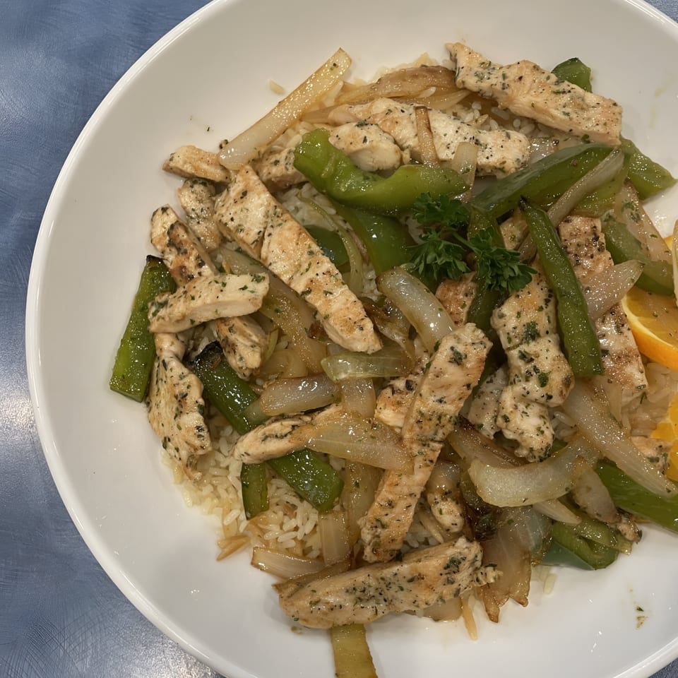 Chicken stir-fry with green peppers and onions over rice, garnished with parsley and an orange slice.