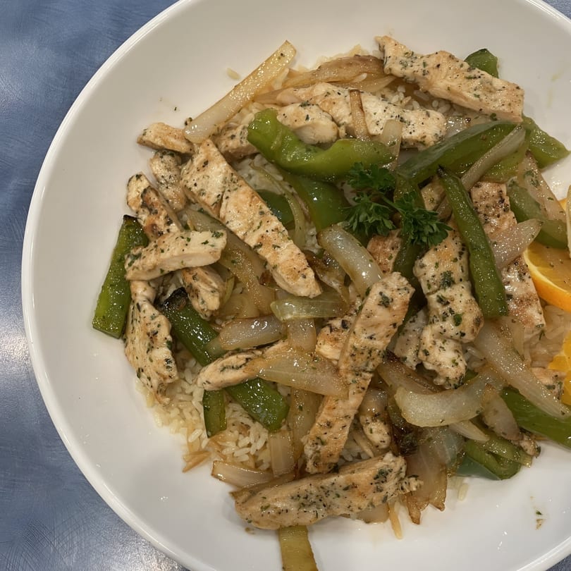 Chicken stir-fry with green peppers and onions over rice, garnished with parsley and an orange slice.