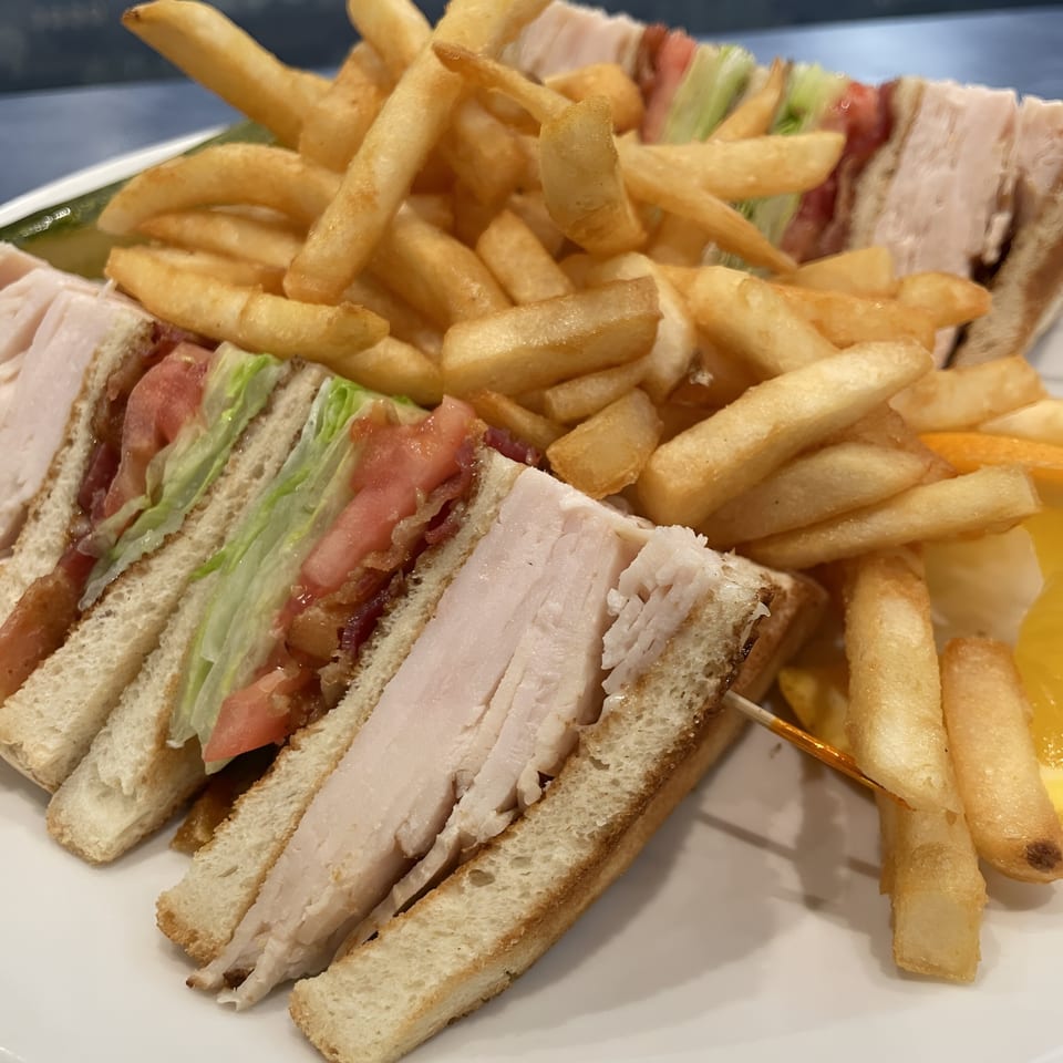 A Sky Diner turkey club sandwich with bacon, lettuce, and tomato, served with golden french fries.