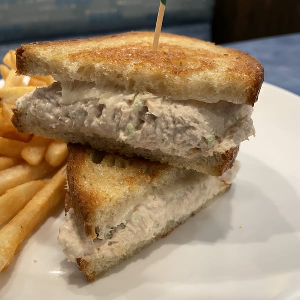 A tuna melt sandwich with golden-brown toasted bread, cut in half, served with a side of fries.