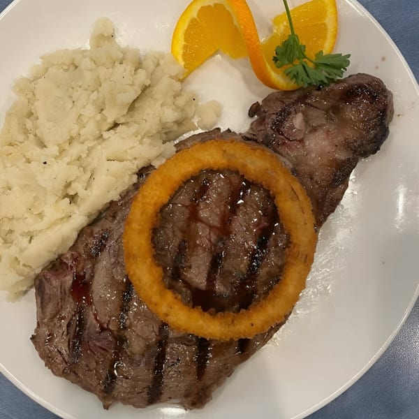 Grilled steak topped with an onion ring, served with mashed potatoes and orange slices.