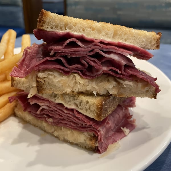 A stacked pastrami and sauerkraut sandwich on toasted bread with a side of golden french fries.