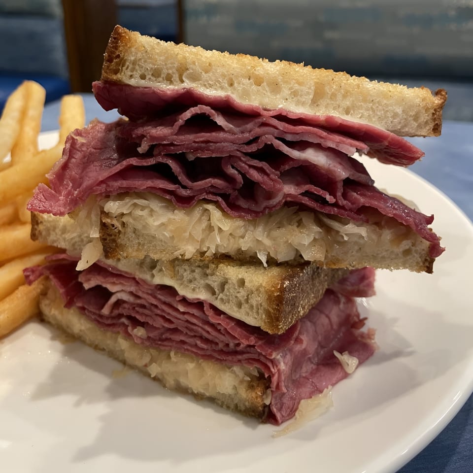 A stacked pastrami and sauerkraut sandwich on toasted bread with a side of golden french fries.