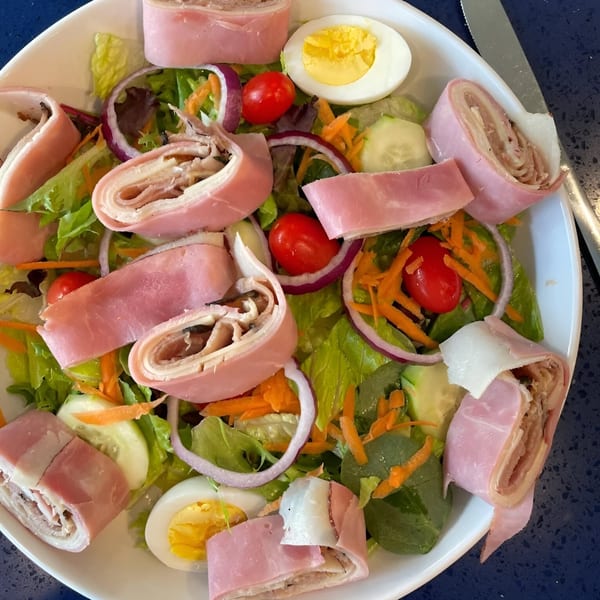 A chef salad with ham and cheese roll-ups, mixed greens, tomatoes, red onion, and hard-boiled egg.