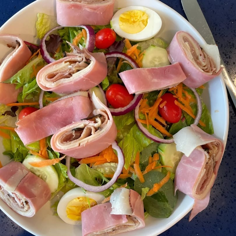A chef salad with ham and cheese roll-ups, mixed greens, tomatoes, red onion, and hard-boiled egg.
